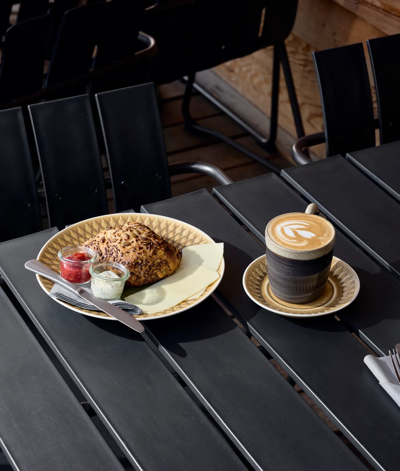 En latte med latte art og en nystegt snurre med jam og creme på en café med sorte stole.