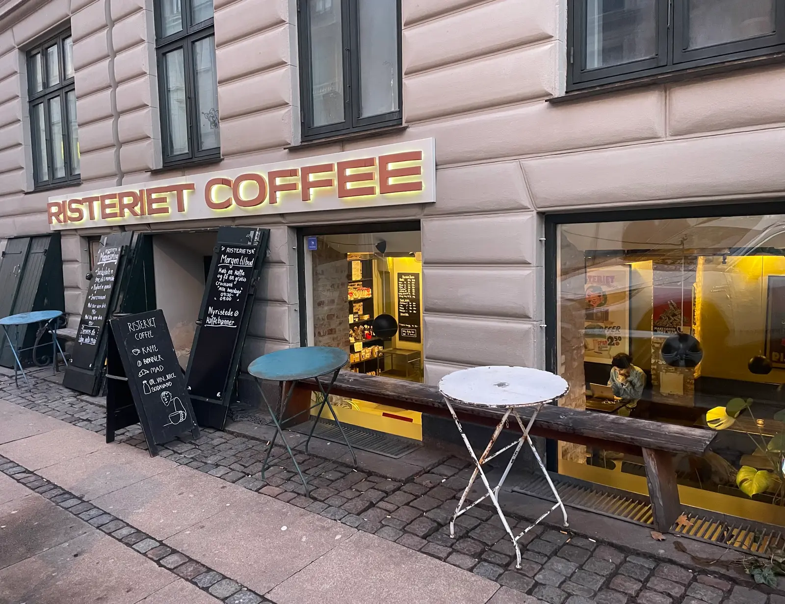 Kaffebar med gul facade og udendørs siddepladser på fortorvet