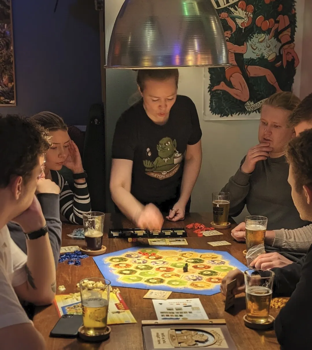 En gruppe venner sidder omkring et træbord og spiller brætspil sammen.