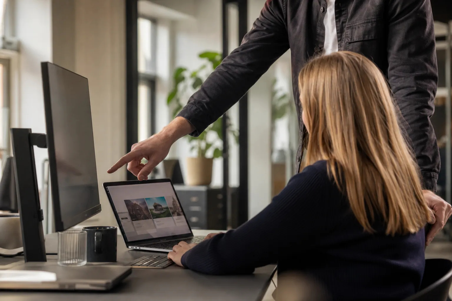 To professionelle diskuterer indholdet på en laptopskærm på et moderne kontor.