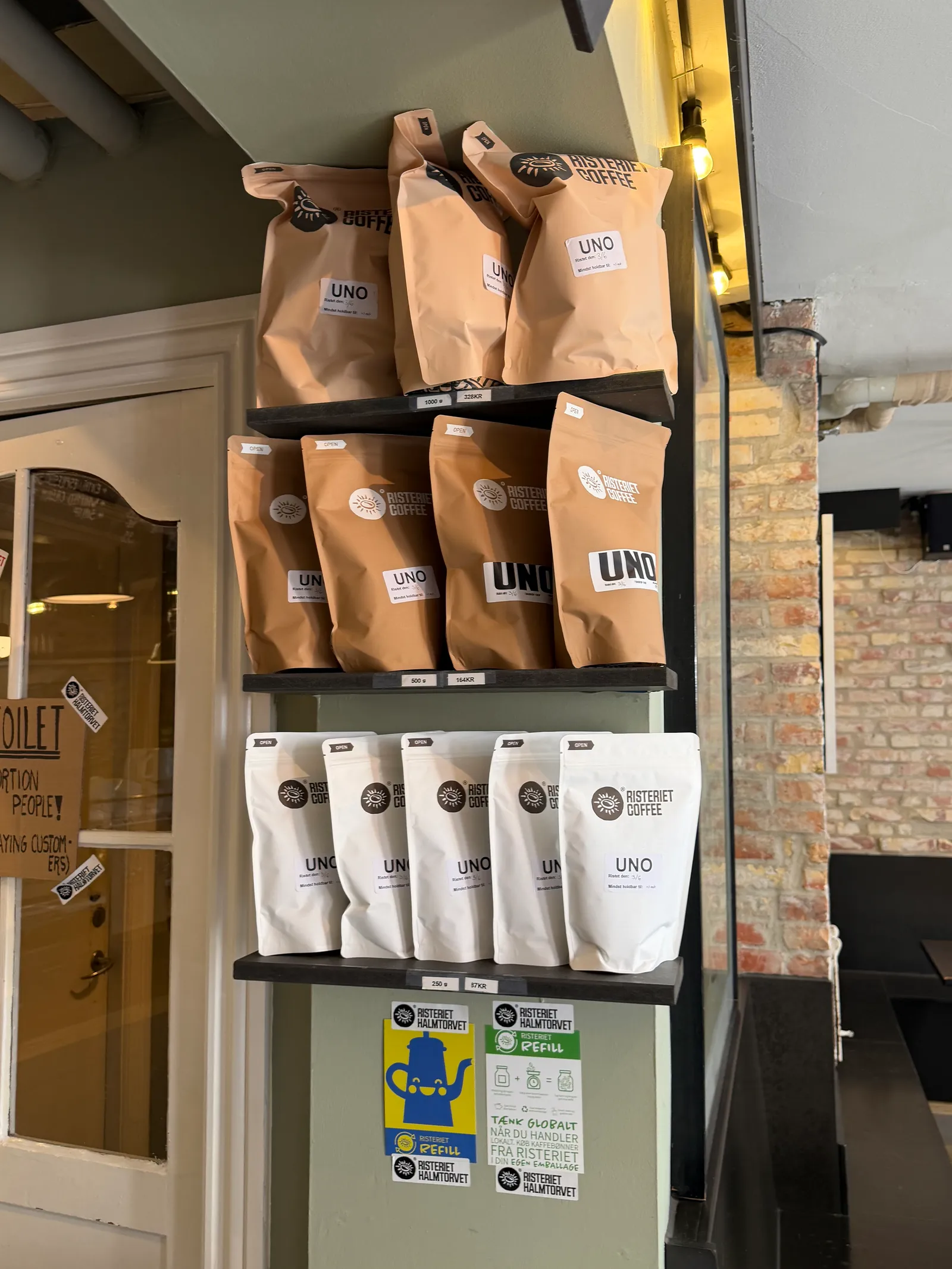 Papirposer med specialty kaffe fra Risteriet står organiseret på sorte butik-hylder i en kaffebar