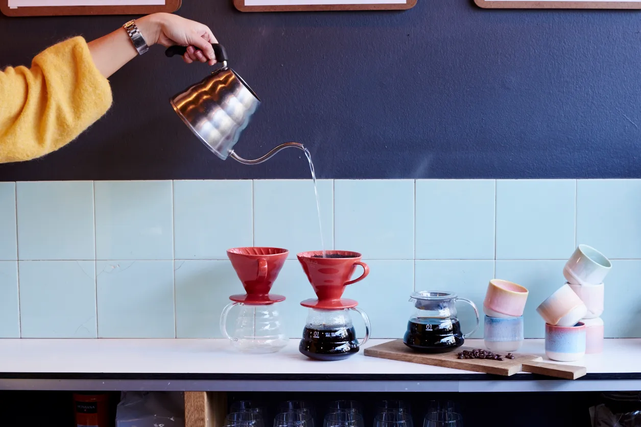 Person hælder varmt vand over rød filtertudse med kaffe.
