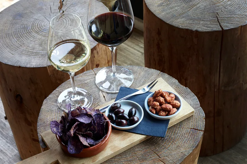 To vinglas med vin og skåle af snacks på træbord.