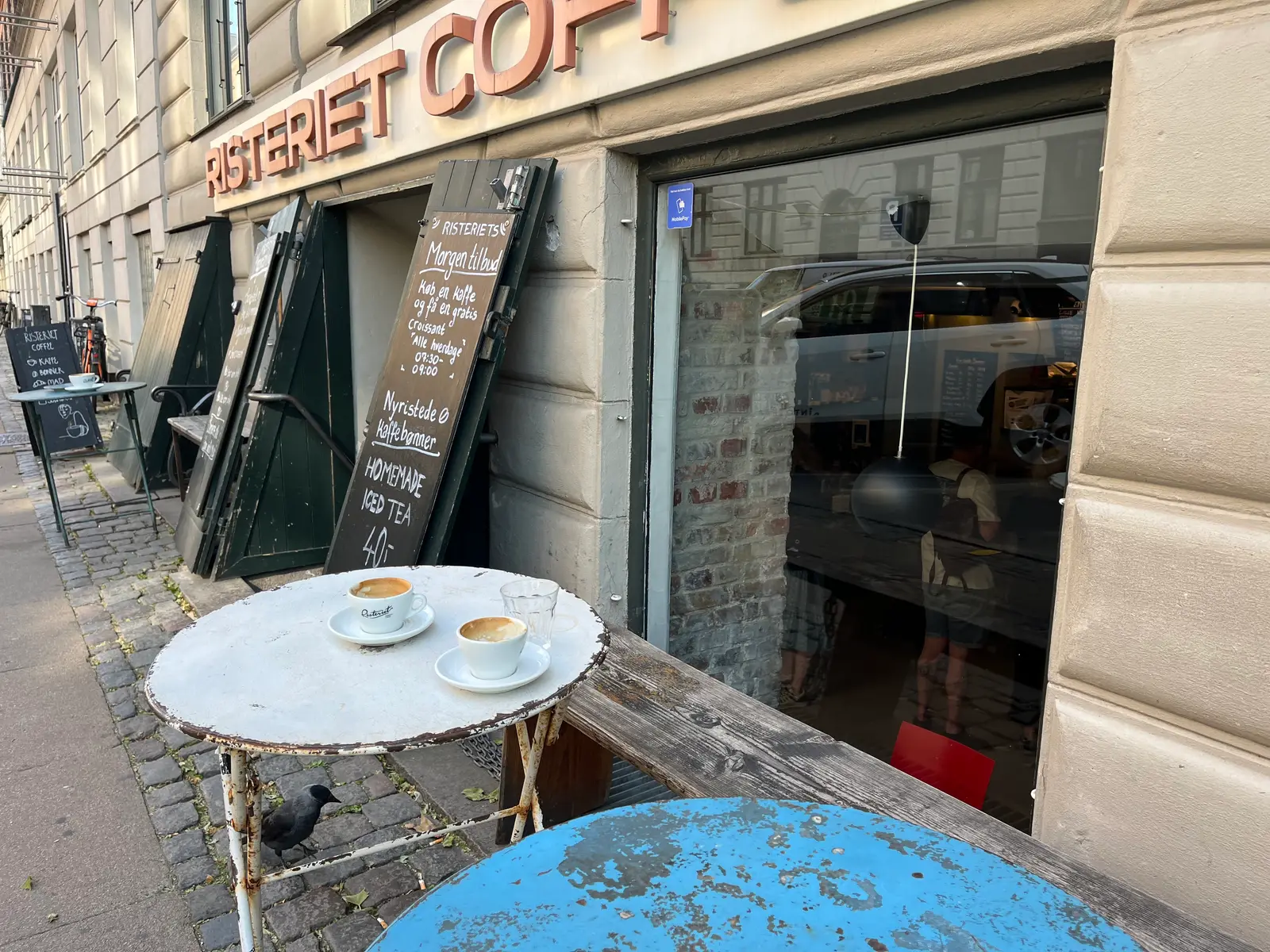 En hyggelig kaffebar med udebord hvor der serveres kaffe med latté kunst.