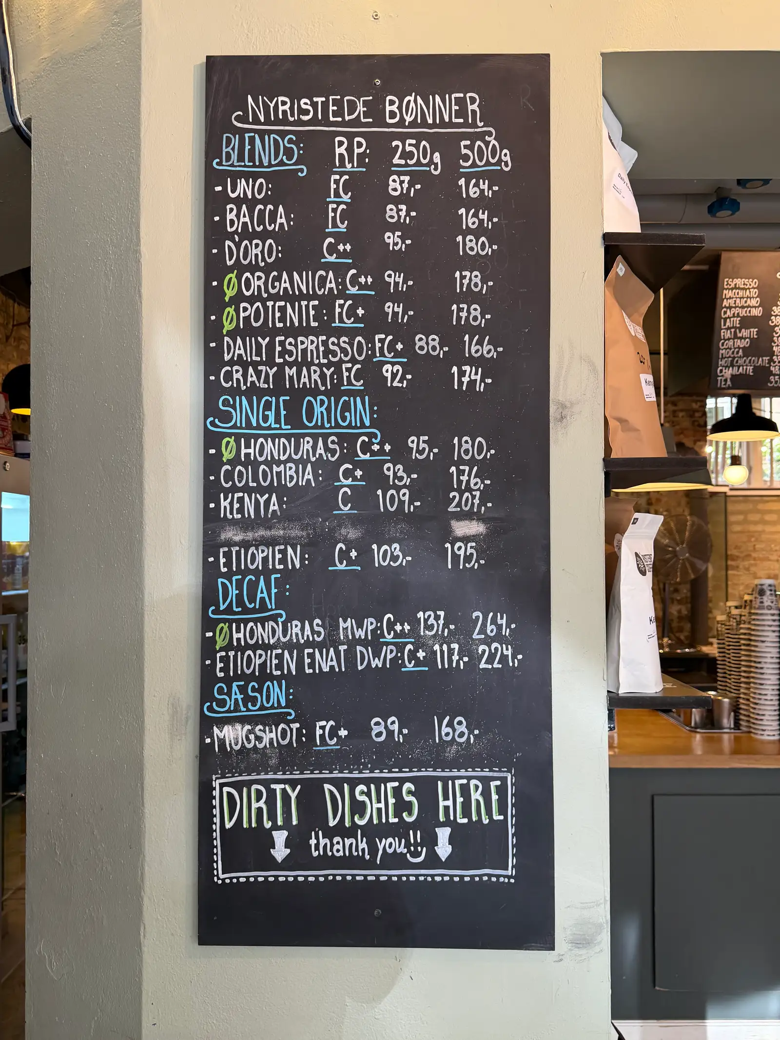 Tavle med handskrevet menuskilt viser forskellige kaffeblandinger og priser i en moderne kaffebar.