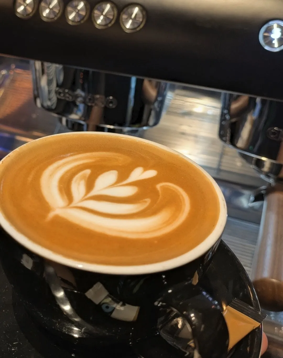 Kaffekop med mørkebrun kaffe og hvidt dekorativt latte art-mønster på toppen.