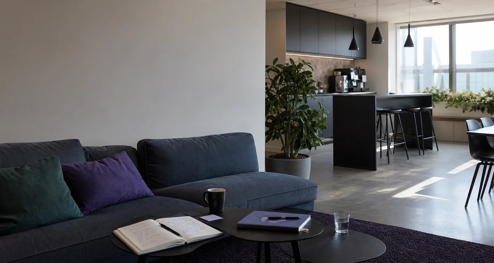 Et åbent kontorrum med sofa, arbejdsbord og professionel køkkencenter.