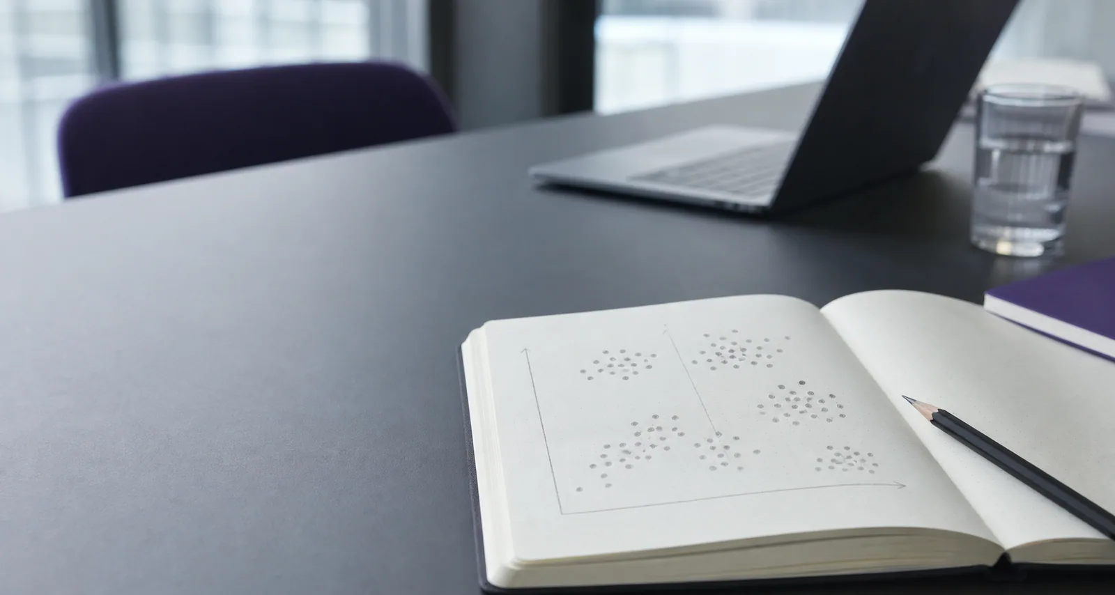 Åben notesbog med datapunkter på et arbejdsskrivebord med laptop i baggrunden