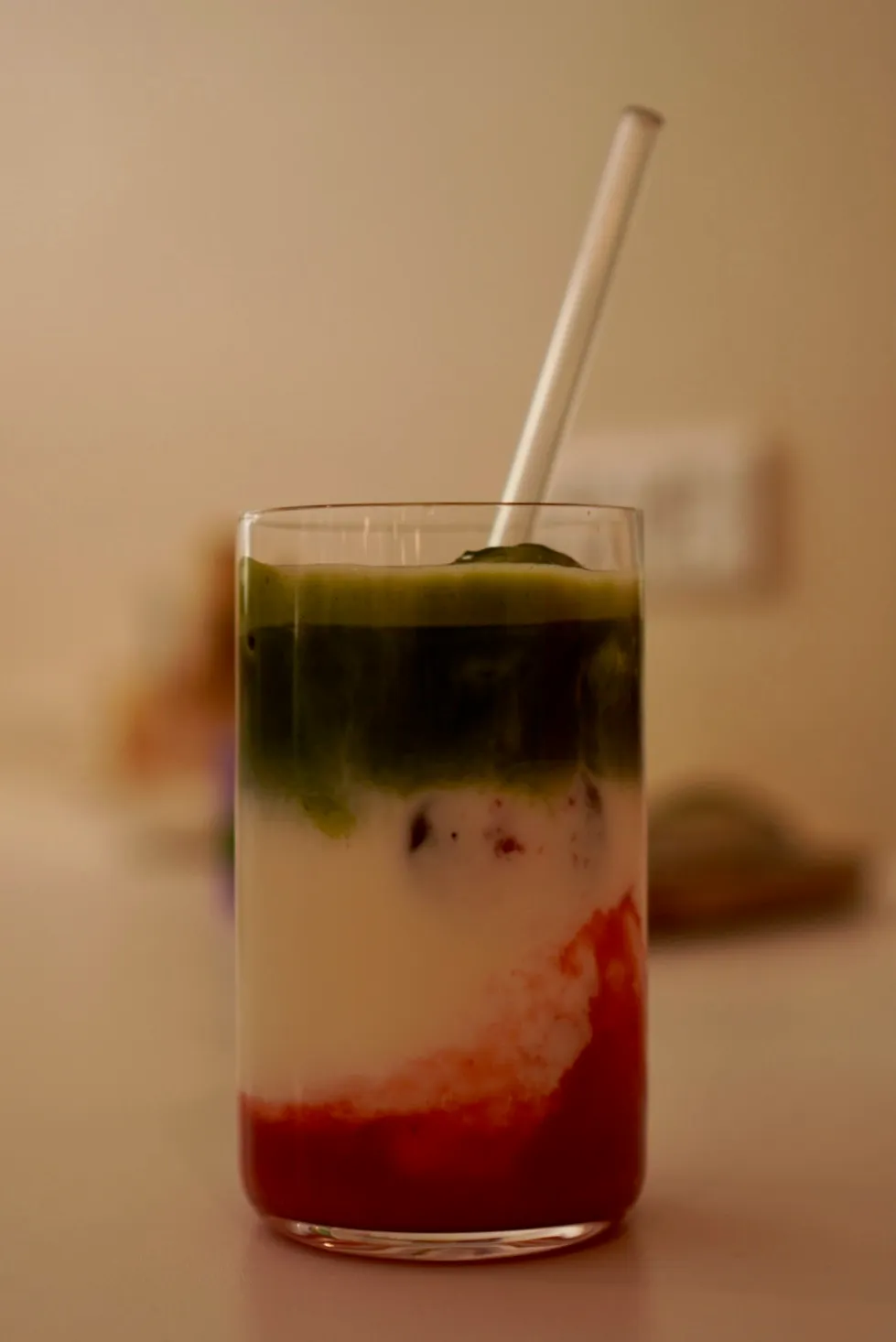 Et glas med en farverig lagdelt cocktail i rødt, hvidt og mørkegrønt med en strå.