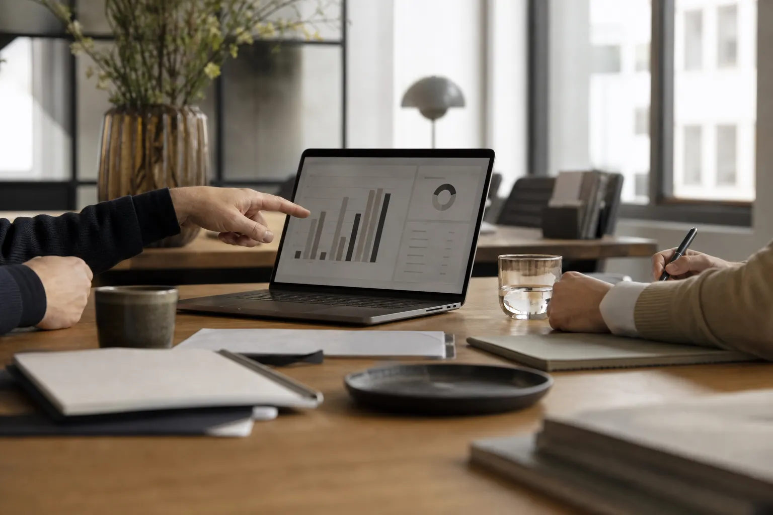 To kollegaer diskuterer analysegrafer på en laptop ved et kontorbord.