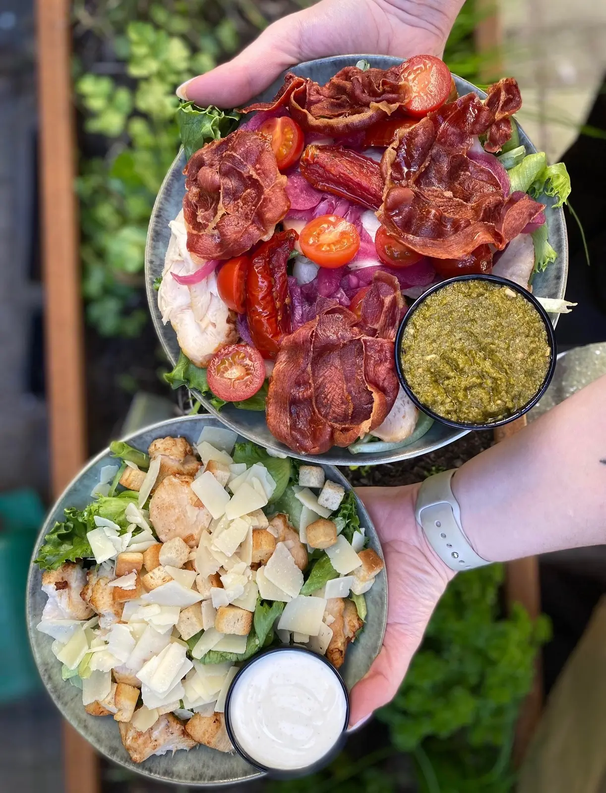 To fine tallerkener med spegepølse, grøn salat, croutons og friske grøntsager serveret udenfor.